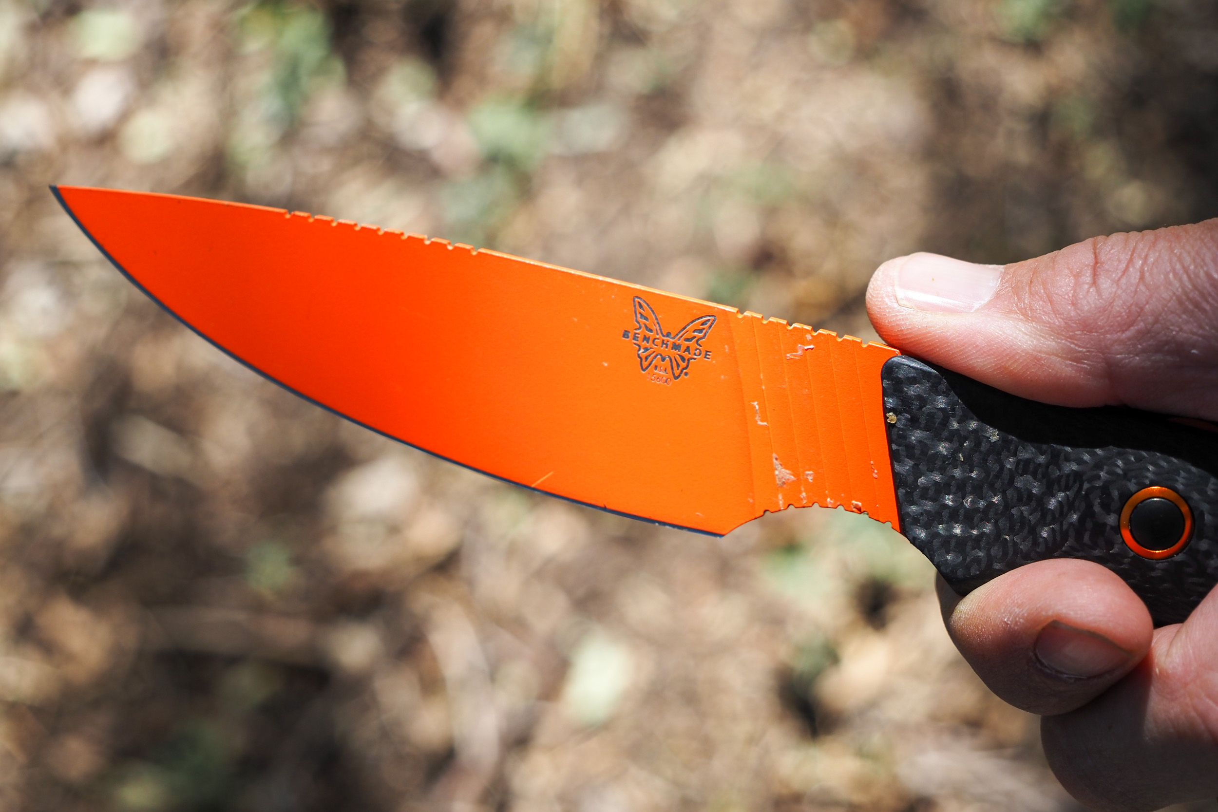 A hand holds a Benchmade Raghorn hunting knife with orange blade
